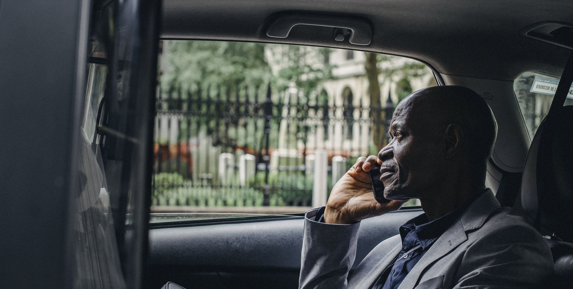 Side view of thoughtful mature African American businessman in elegant suit talking on smartphone while riding on passenger seat of taxi